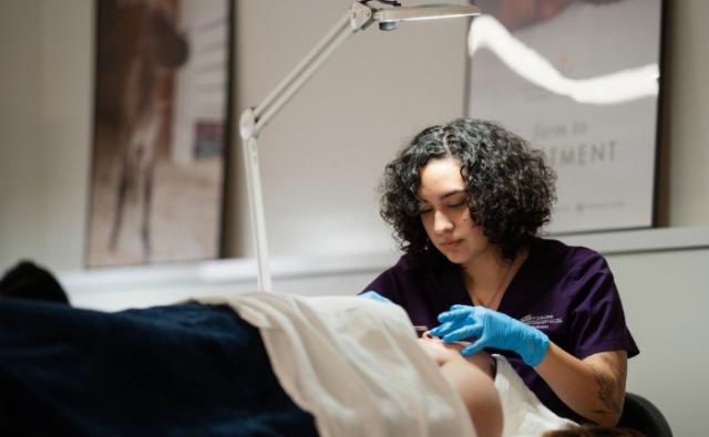 Aesthetician student performing a facial assessment under a magnification lamp