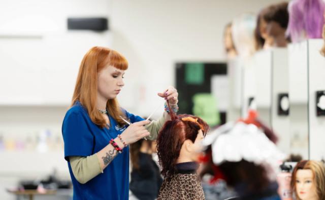 Student practicing precise haircutting and sectioning techniques on a mannequin in a cosmetology class