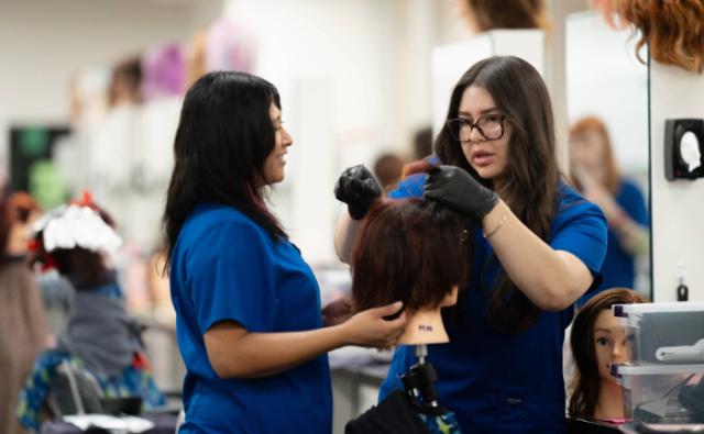 Cosmetology students practicing hair styling on a mannequin head