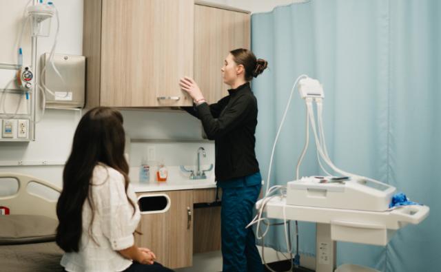 Healthcare worker and patient inside a clinical exam room with diagnostic monitoring equipment