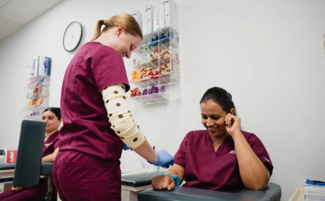 Healthcare student applying a tourniquet to a classmate during phlebotomy training