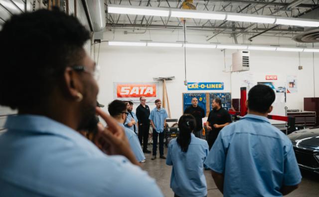 Students listening to an instructor lecture in an automotive repair shop