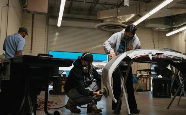 Students sanding a vehicle bumper on a stand in a body repair shop