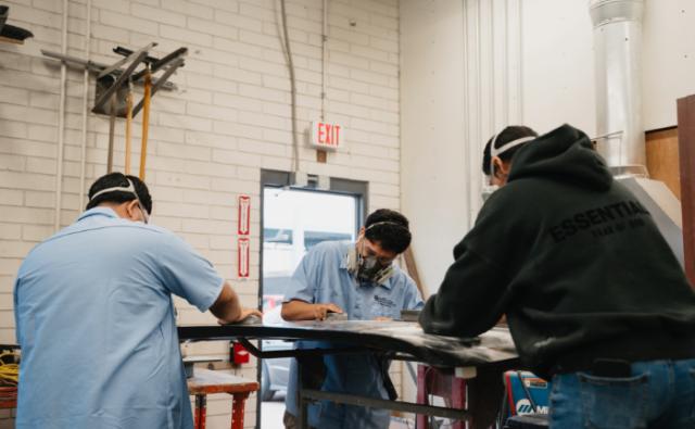 Students prepping and sanding a car panel in an auto body lab