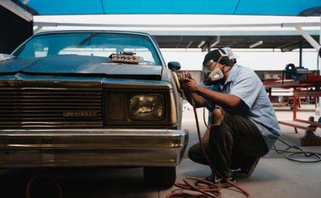 Student sanding a vehicle body panel with protective gear