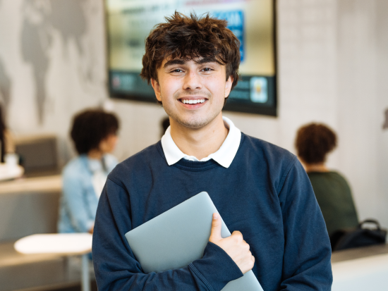 Young male holding laptop wearing blue sweatshirt and white button down